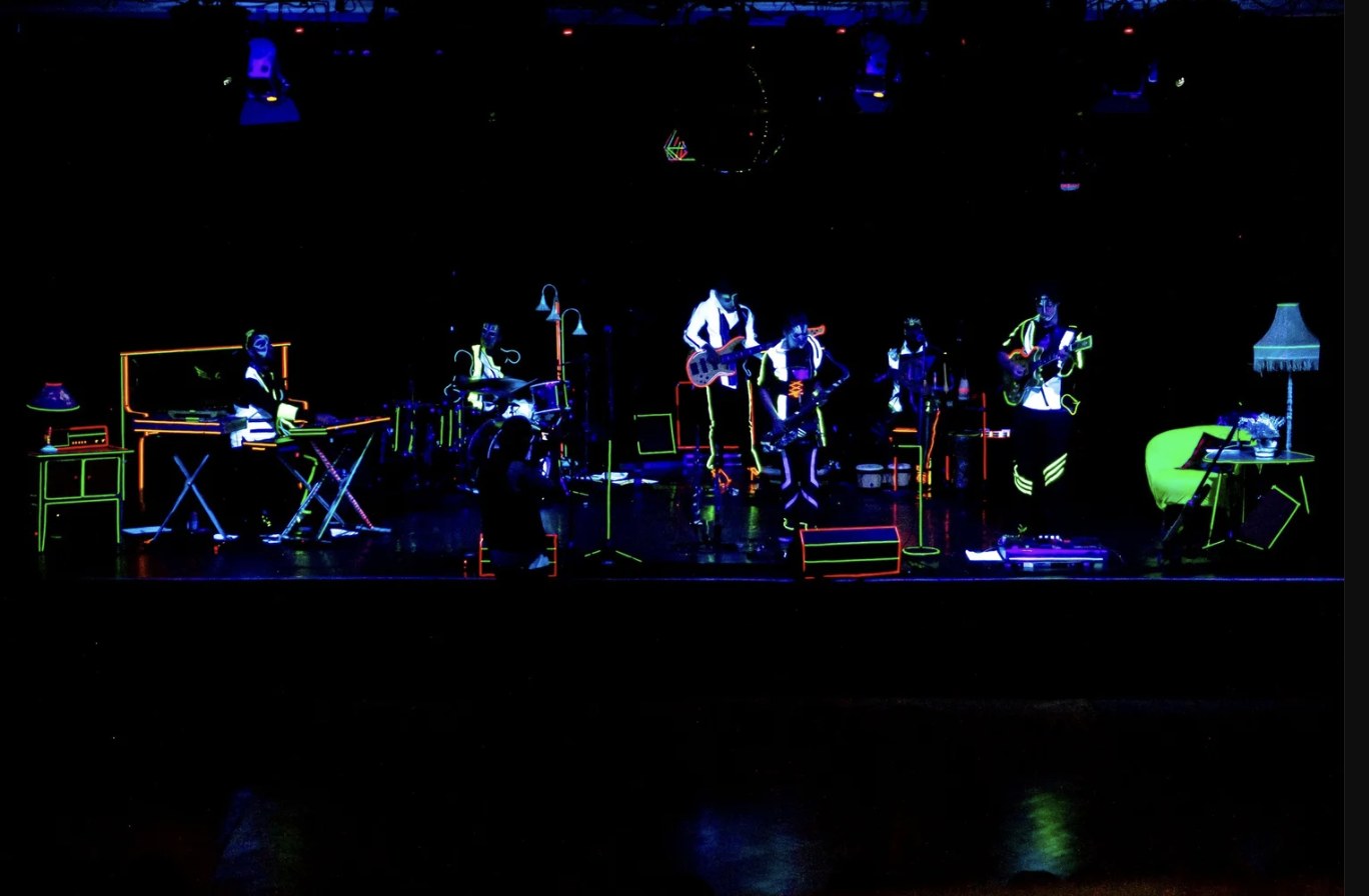 Out Of Nations performing under black light, full band and stage lit in neon outlines